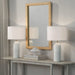 Two white table lamps on a wooden console table with a mirror above, against a gray wall.