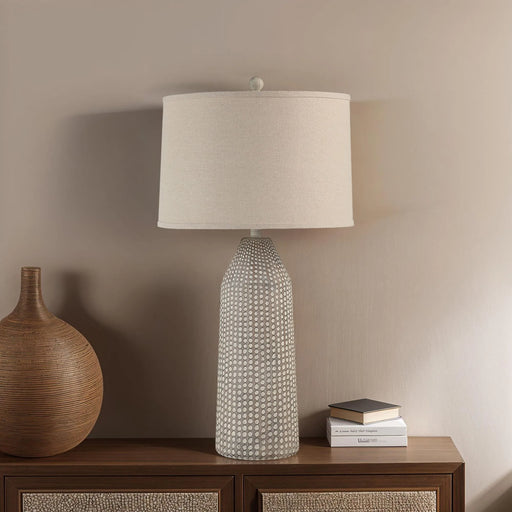 Decorative lamp with textured base on a wooden sideboard against a beige wall