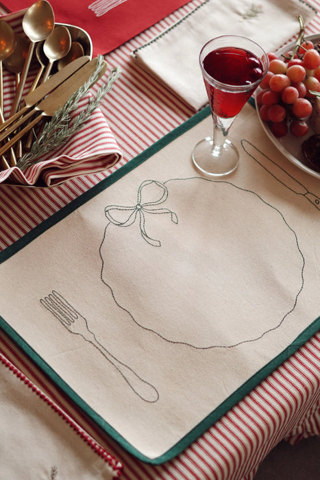 Natural cotton placemat with green embroidered cutlery, plate and bow on a red and white striped tablecloth