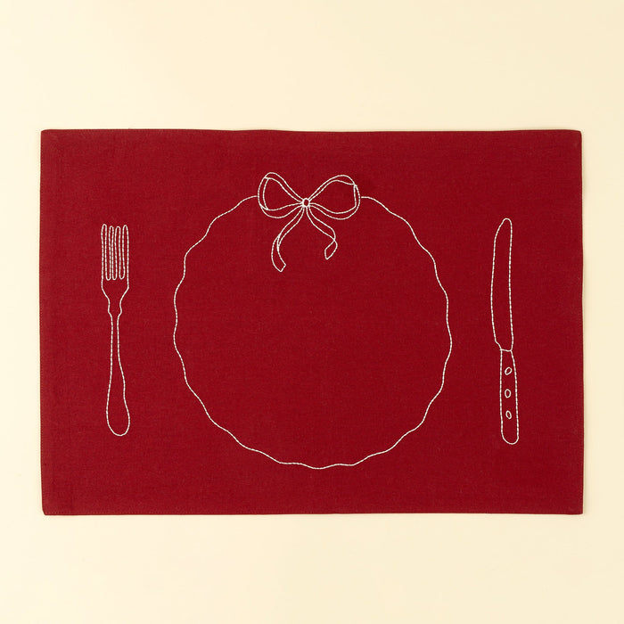 Indaba red cotton placemat with white embroidery outlining a plate, ribbon bow, fork and knife