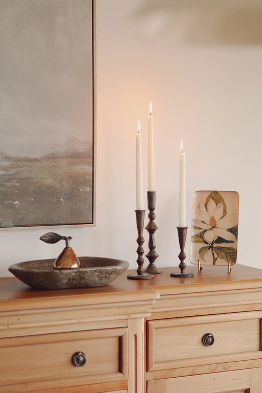 Decorative bronze pear on a tray beside tall candle holders on a wooden console