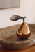 Bronze mercury-glass pear with a textured brass leaf resting in a shallow decorative tray