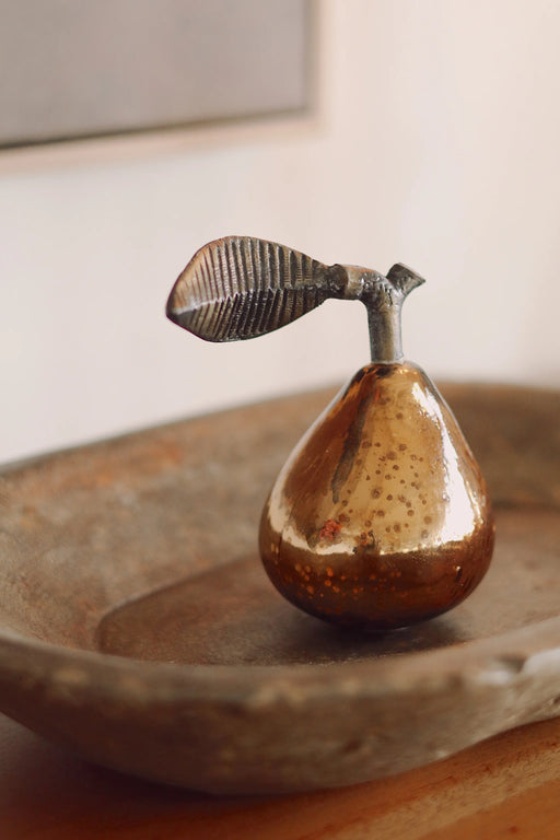 Bronze mercury-glass pear with a textured brass leaf resting in a shallow decorative tray