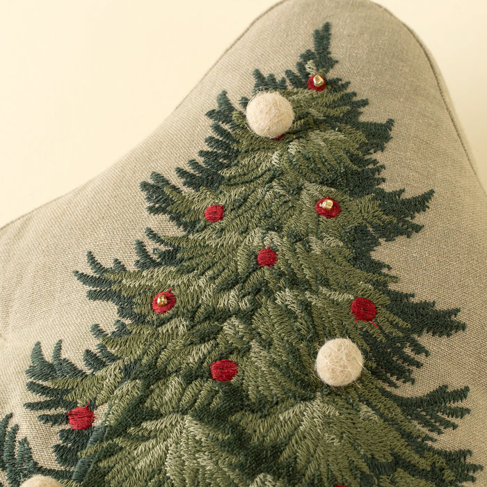 Close-up of embroidered green branches with red decorations and raised cream embellishments on the Christmas tree pillow