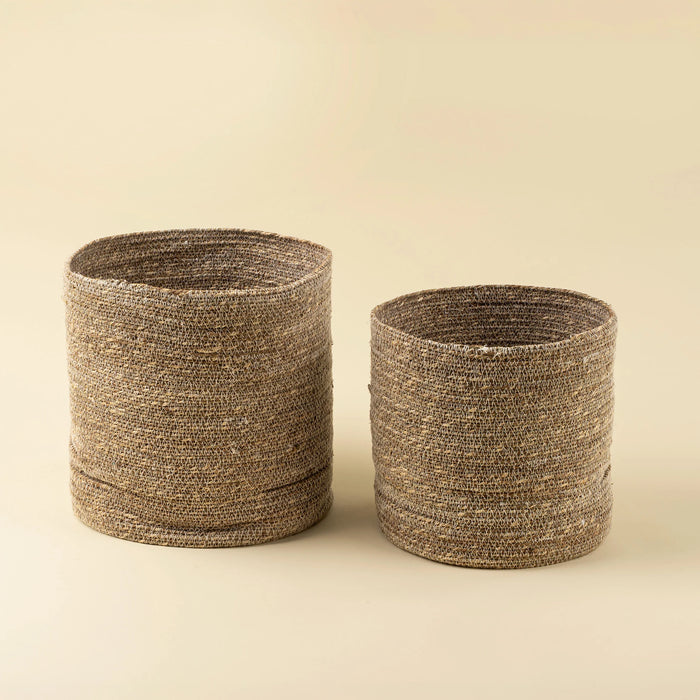 Two cylindrical natural seagrass baskets in different sizes with white zigzag stitching