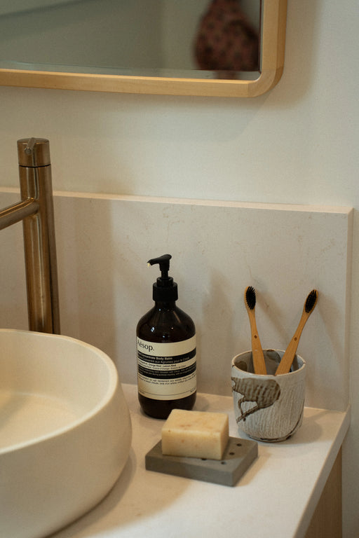 Bathroom counter styled with a concrete soap dish, pump dispenser and toothbrush holder beside the basin