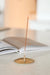Incense stick in a gold-toned holder beside an open book on a light tabletop