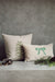Green bow lumbar pillow beside a square Christmas tree cushion against a grey wall with seasonal greenery