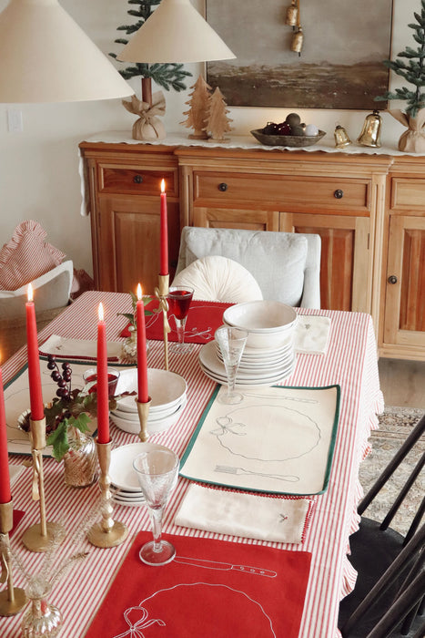 Dining table styled with green-edged placemats, white dinnerware and red candles