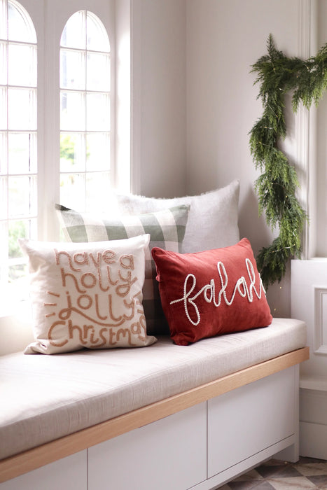Jolly Christmas pillow beside a red cushion on a window seat with evergreen garland