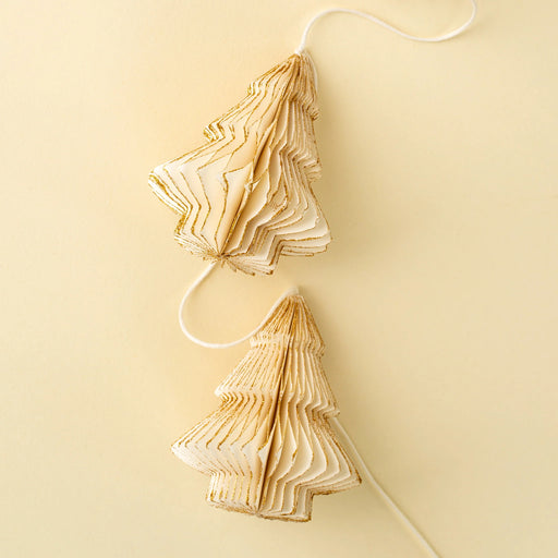 Close-up of ivory paper trees with layered folds and antique gold edges attached to a pale garland cord
