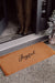 Joyful coir doormat at a dark front doorway beside a frosted miniature Christmas tree