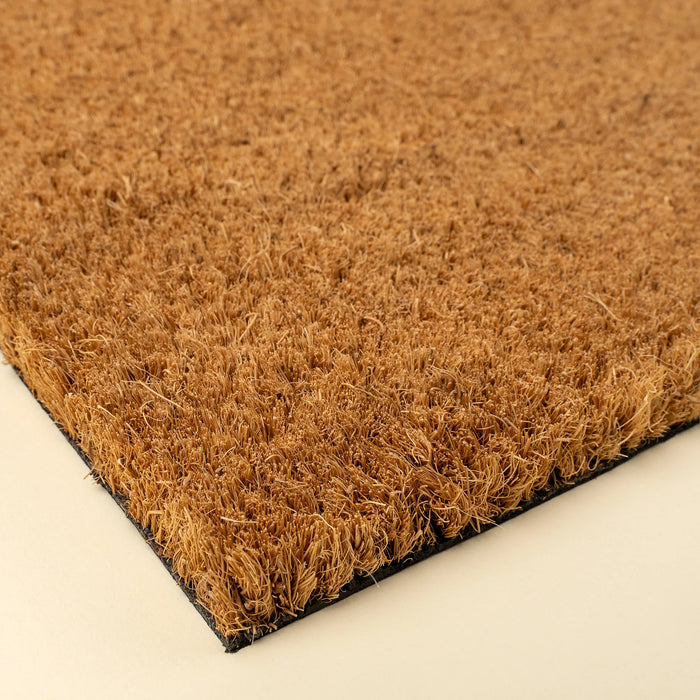 Corner detail of the Joyful doormat showing textured brown coir fibres above a thin black PVC backing