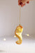 Hand holding an Indaba lemon twist glass ornament by its gold cord, with glittered yellow rind and blurred lights behind