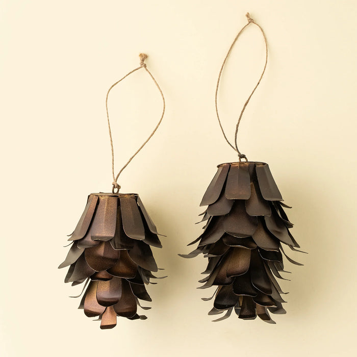 Two bronze pinecone ornaments with overlapping iron scales and natural cord loops against a cream background