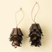 Two bronze pinecone ornaments with overlapping iron scales and natural cord loops against a cream background