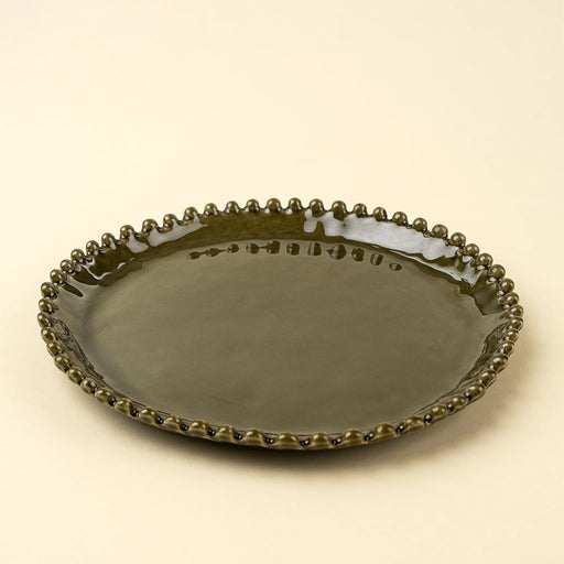 Angled view of a Merida green dinner plate showing its raised edge and decorative hobnail rim