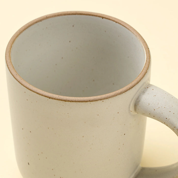 Close-up of an Indaba Rowe ivory mug showing its speckled interior, unglazed rim and curved handle