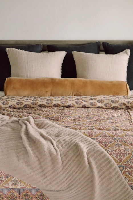 Tuffet Snug Throw draped across patterned bedding beneath cream pillows and a mustard bolster cushion