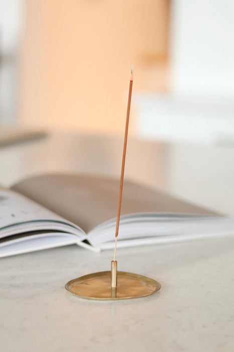 Incense stick standing in a gold-toned holder beside an open book