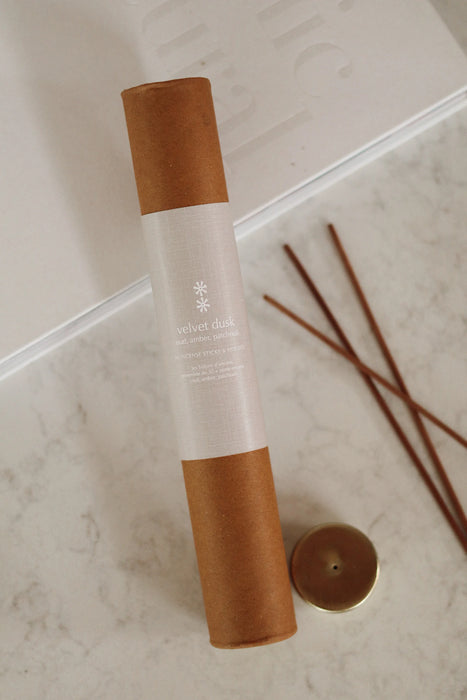 Velvet Dusk incense tube with a cream label beside loose incense sticks and a gold-toned holder