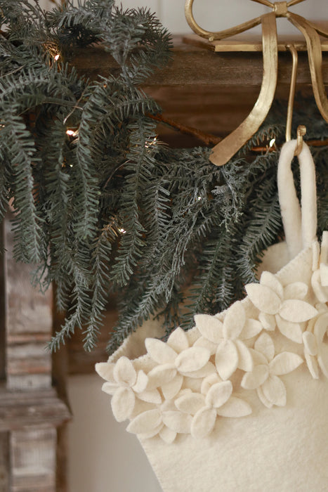 Close-up of the stocking’s felt hanging loop and layered cream flowers beside evergreen branches